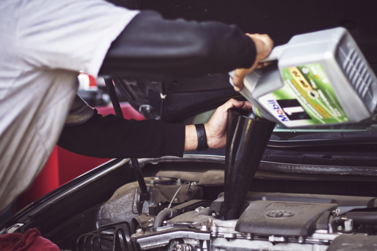 Pessoa despejando óleo novo no motor de um carro durante troca de óleo